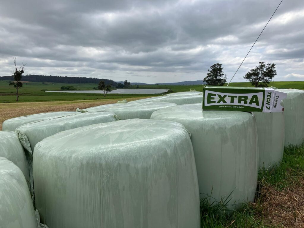 Tractor applying silage wrap on harvested bales.